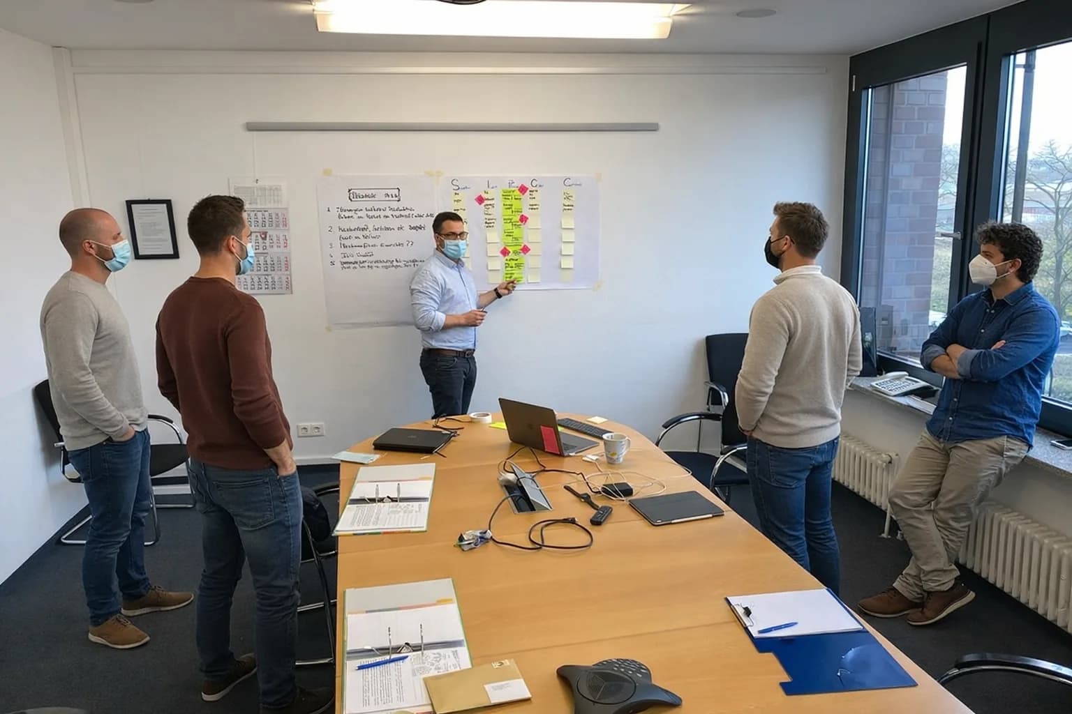 Workshopteam steht gemeinsam vor einem SIPOC-Board im Besprechungsraum.